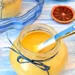 Open jar of blood orange curd with spoon inside.