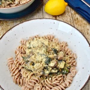 Two bowls of mushroom and chard pasta, a lemon and two forks resting on a navy coloured napkin.