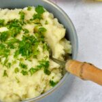 Bowl of vegan parsnip and potato mash with spoon and parsley.