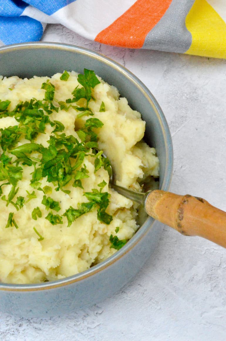 Bowl of vegan parsnip and potato mash with spoon and parsley.