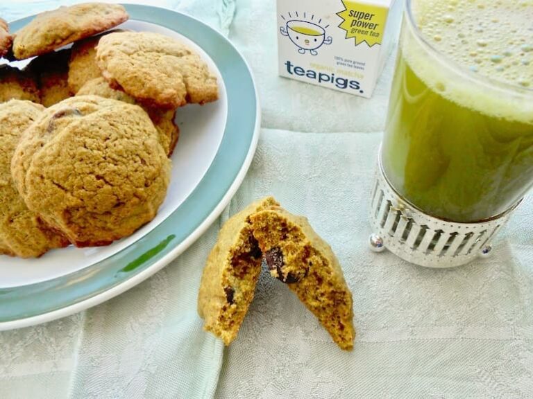 A glass of matcha green tea with a plate of matcha chocolate chip cookies and one broken in half.