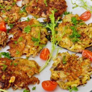 Oca Latkes on a grey plate with chopped parsley and tomato quarters scattered around.