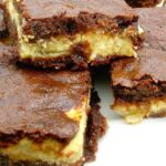 A plate of apple cheesecake brownies stacked on top of each other.
