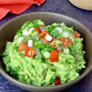 A bowl of simple homemade guacamole topped with diced tomatoes, jalapeño and cilantro.