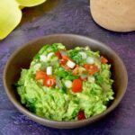 A bowl of simple homemade guacamole with various toppings.
