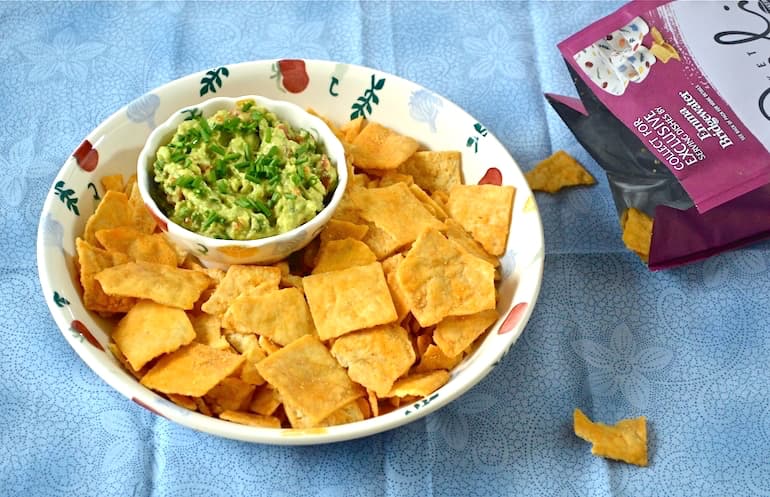 A small bowl of simple homemade guacamole sitting in a large bowl of corn chips.