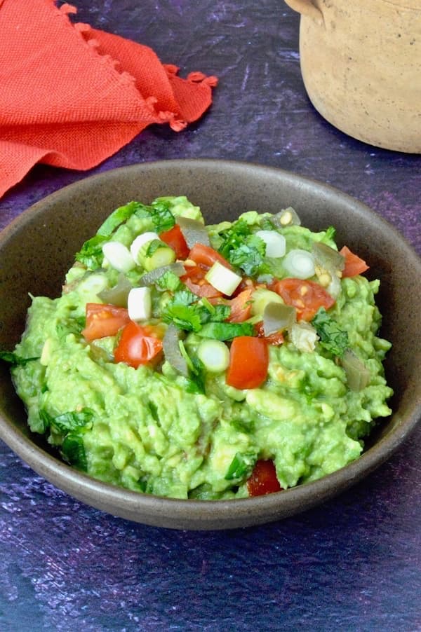 A bowl of simple homemade guacamole topped with diced tomatoes, jalapeño and cilantro.