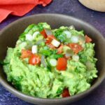 Bowl of simple homemade guacamole topped with diced tomatoes, jalapeño and cilantro.