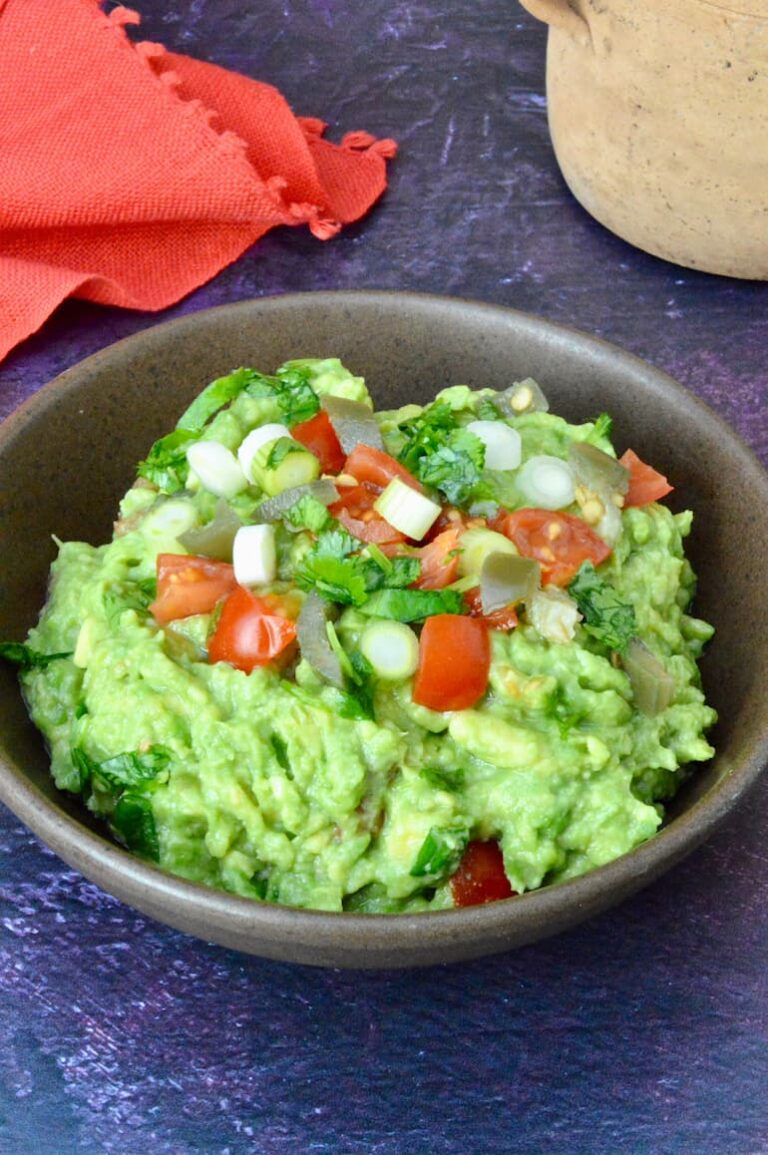 Bowl of simple homemade guacamole topped with diced tomatoes, jalapeño and cilantro.