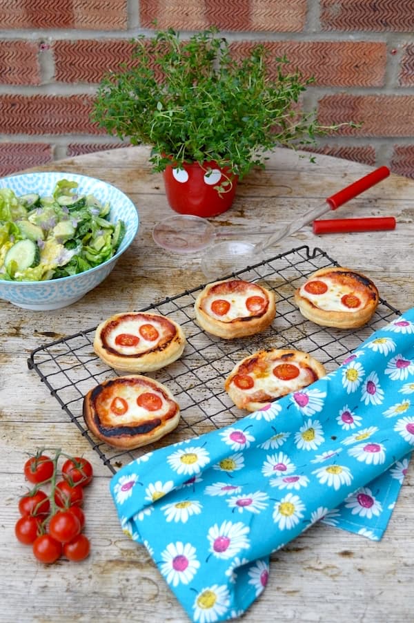 Five puff pastry pies cooking on a wire rack with a bowl of green salad, some tomatoes and a pot of thyme.