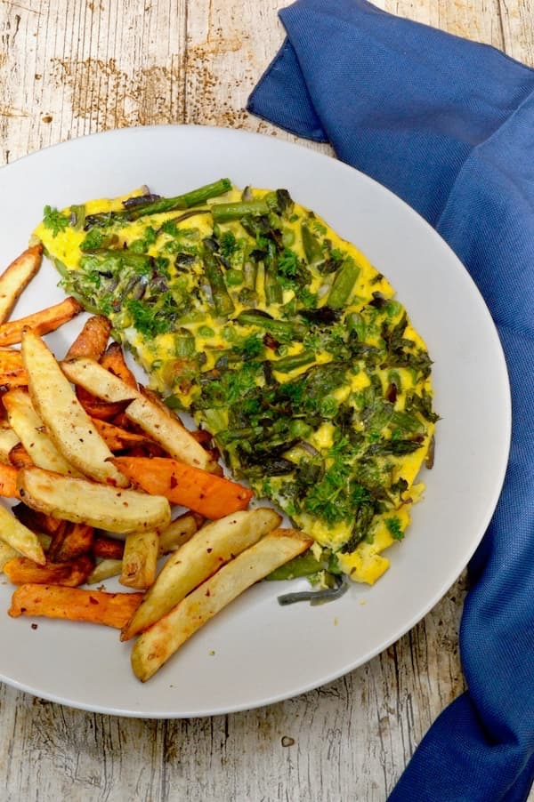 A half slice of asparagus, pea and mint frittata on a grey plate with chips.