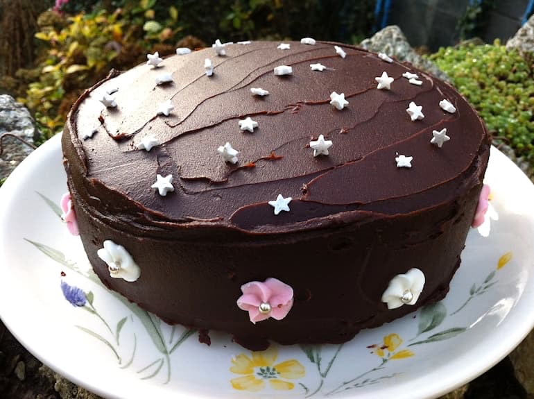 A chocolate fudge cake with ganache frosting and decorated with stars and flowers.