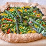 Green vegetable galette on a board with a slice slightly removed.