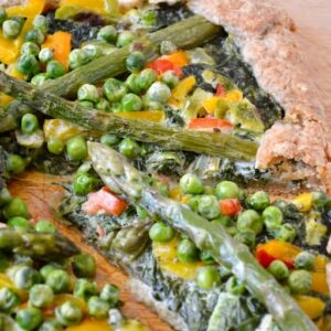 Green vegetable galette on a board with a slice slightly removed.