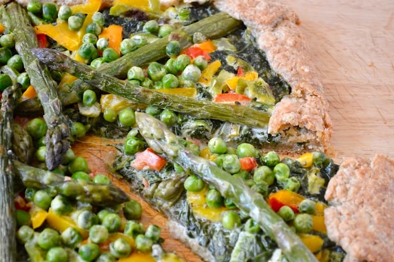 Green vegetable galette on a board with a slice slightly removed.