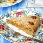 Jam almond cake slice sandwiched with plum jam on a floral plate with fork.