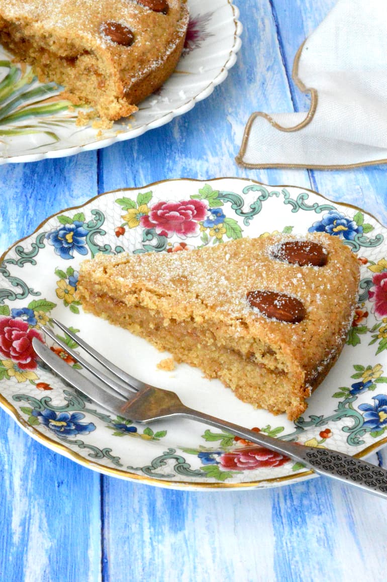 Jam almond cake slice sandwiched with plum jam on a floral plate with fork.