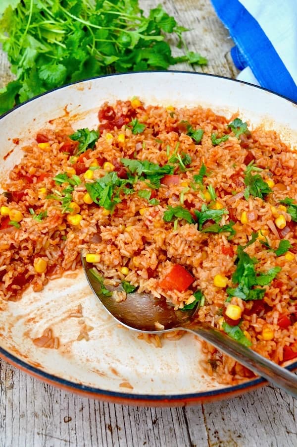 A dish of tomato Mexican brown rice with serving spoon and some removed.