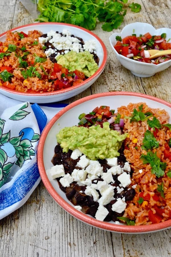 Two rice bowls filled with Mexican brown rice, black beans and feta, smashed avocado and fresh salsa.