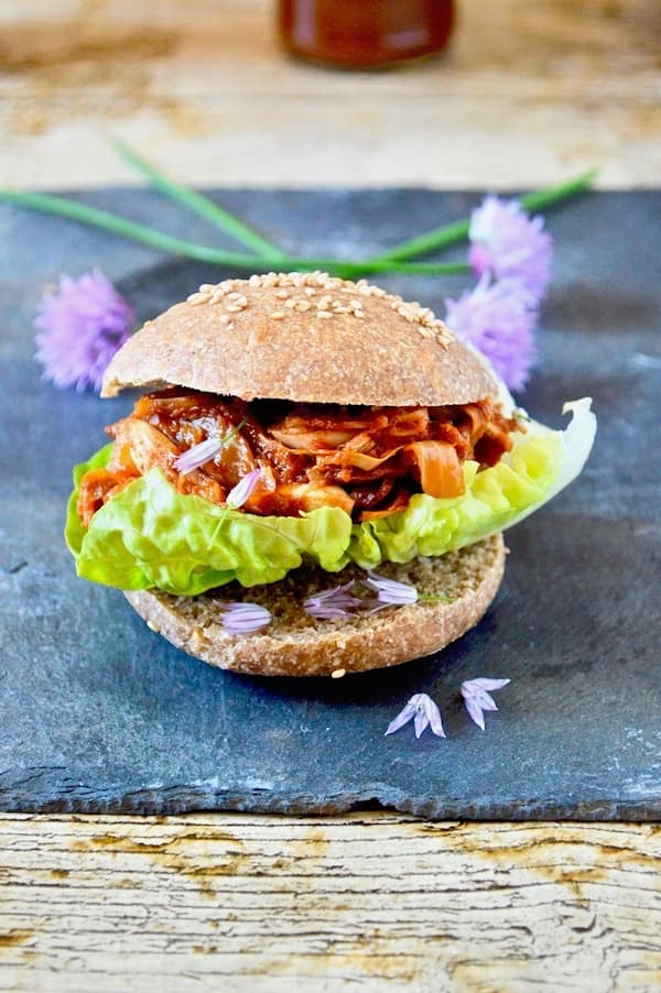 Pulled Jackfruit in Homemade Barbecue Sauce in a wholemeal burger bun with lettuce. Chive flowers in the background.