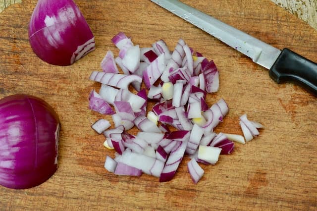 A chopped red onion on a chopping board with one part of it finely diced.