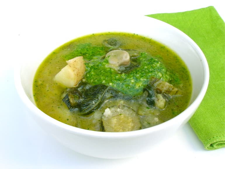 A bowl of chunky green summer soup with parsley and almond pesto. A green napkin on the side.