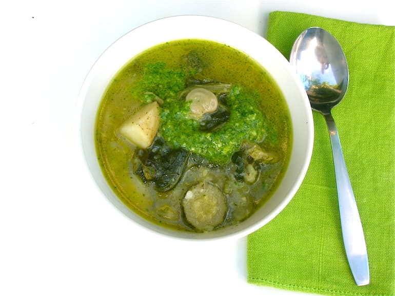A bowl of chunky green summer soup with parsley and almond pesto. A spoon and napkin on the side.