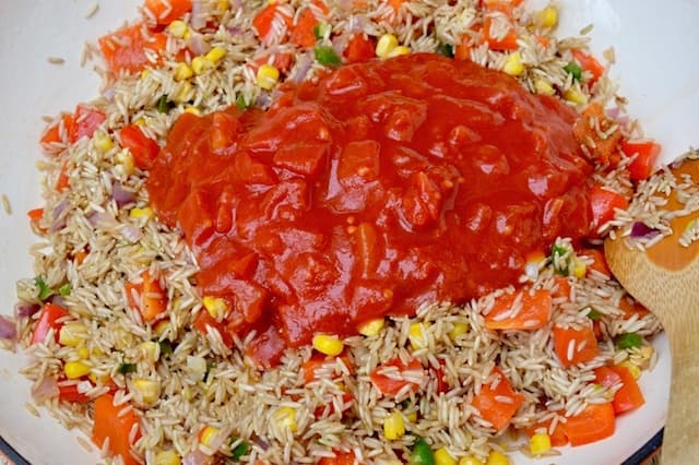 Rice and Mexican vegetables frying in a pan with a tin of chopped tomatoes on top.