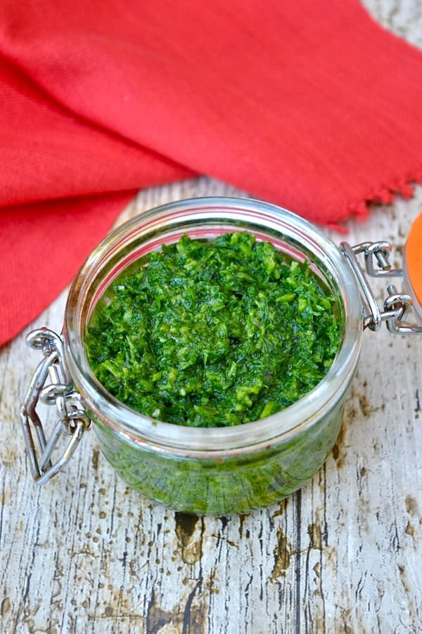 Open jar of homemade vibrant green carrot top pistou with a red napkin in the background.