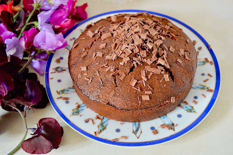 Chocolate lime cake topped with sea-salted chocolate shavings alongside a bunch of sweet peas.