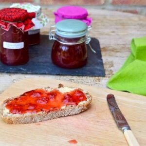 A slice of bread spread with butter and easy homemade strawberry jam, with jars of it in the background.
