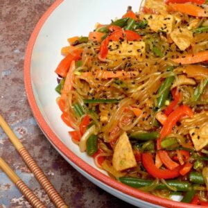 Half a bowl of Korean glass noodles with tempeh and vegetables (japchae).