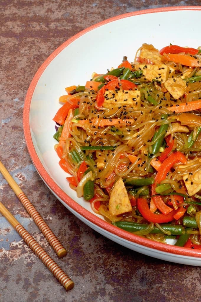 Half a bowl of Korean glass noodles with tempeh and vegetables (japchae).
