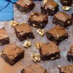 Real chocolate brownies on a baking tray with walnuts scattered about and a blue napkin in the background.