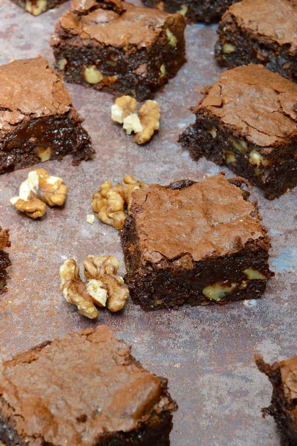 Real chocolate brownies on a baking tray with walnuts scattered about.