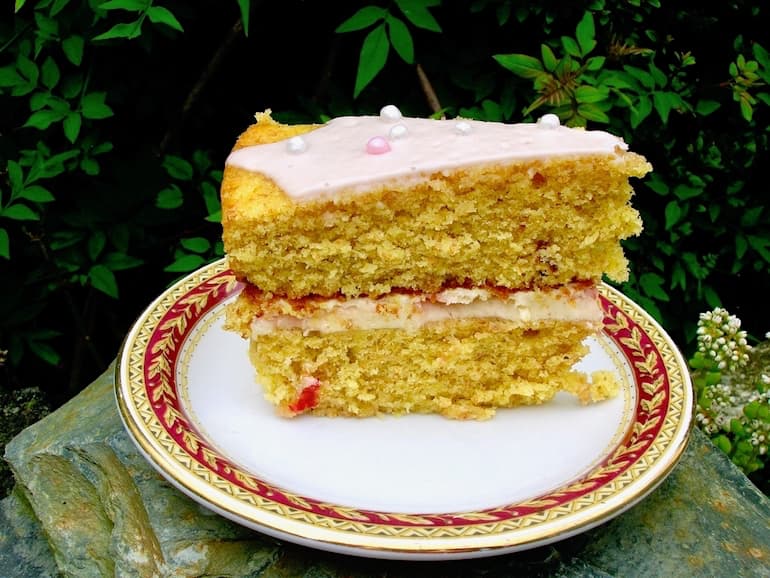 A slice of rose strawberry Victoria sponge cake on a plate on a garden wall.