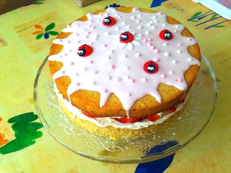 Rose strawberry Victoria sponge cake decorated with ladybirds on a glass cake stand.