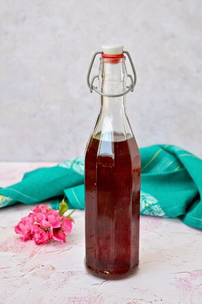 Bottle of homemade rose syrup with a turquoise cloth and pink rose in the background.