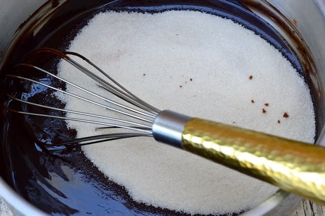 Whisking sugar into cocoa batter with a gold handled whisk.