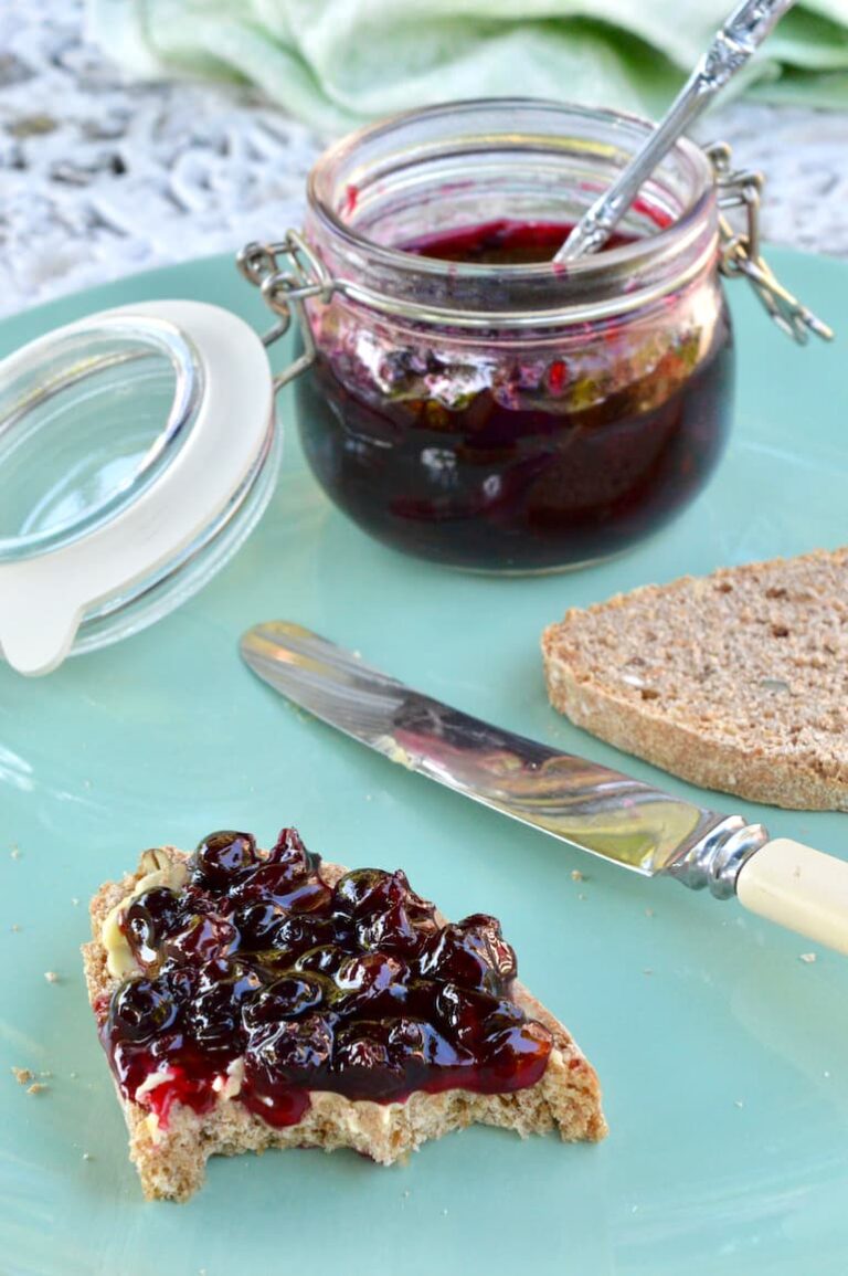 Homemade blackcurrant jam in open jar and spread on bread and butter.