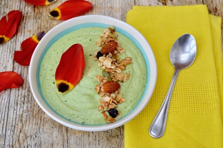 Double Pear & Almond Green Smoothie Bowl with a line of granola and flower petals.
