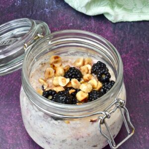 A clip top jar of blackberry overnight oats with toasted hazelnuts and honey drizzled over the top.
