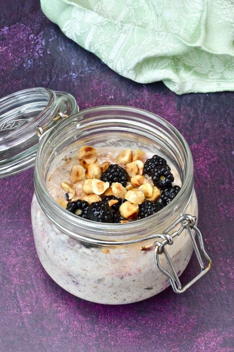 A clip top jar of blackberry overnight oats with toasted hazelnuts and honey drizzled over the top.