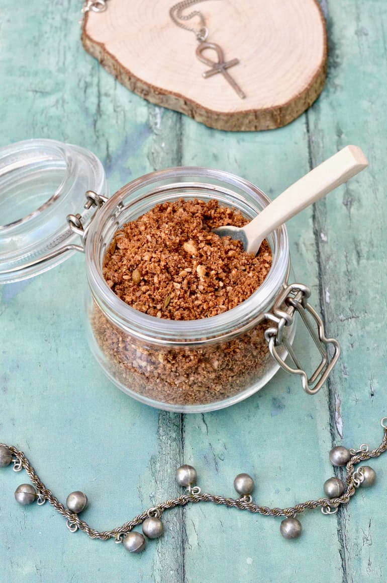 Open jar of Egyptian dukkah spice mix with spoon sticking out.