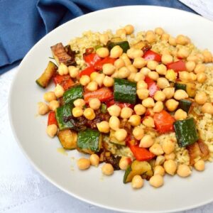 A grey plate of chilli chickpeas, herbed peppers and courgettes on a bed of freekeh.