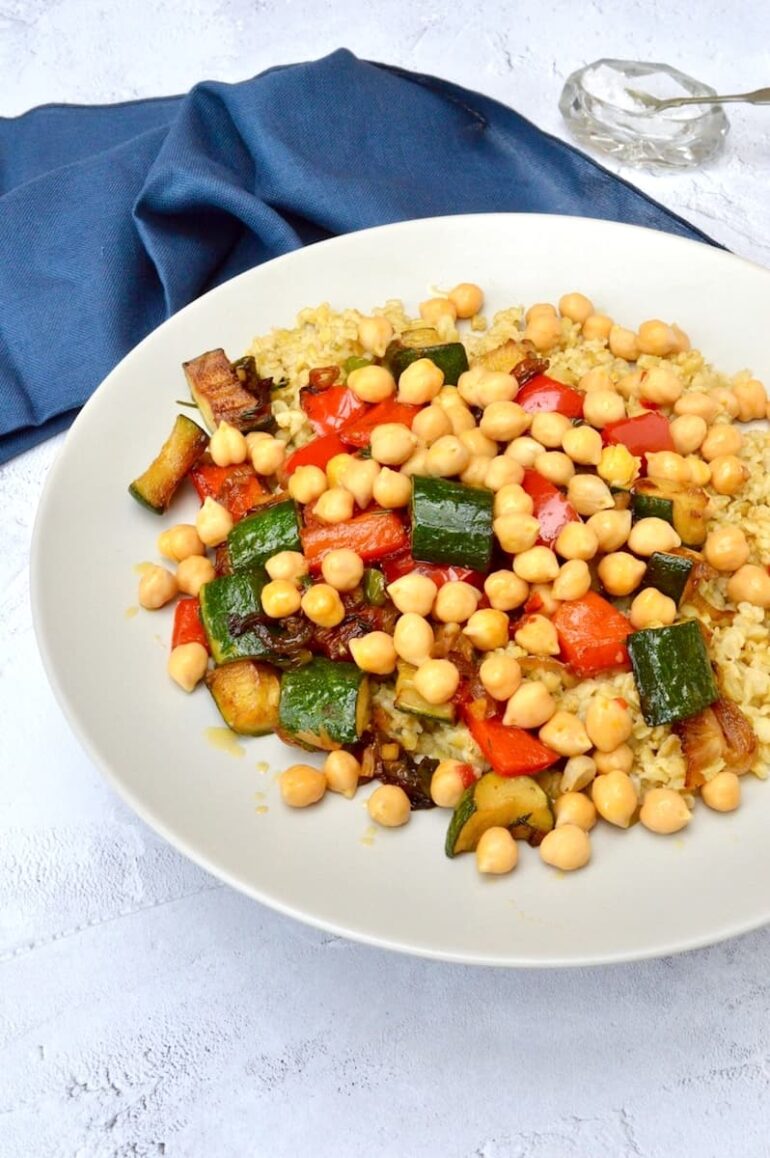 A grey plate of chilli chickpeas, herbed peppers and courgettes on a bed of freekeh.