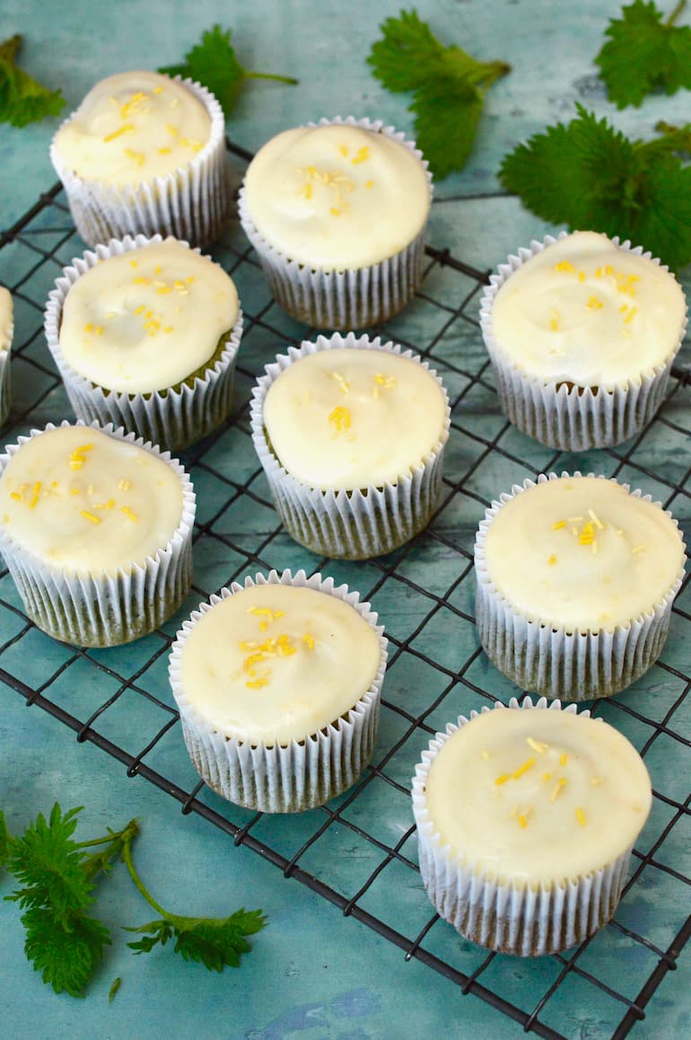 Rack of lemon and white chocolate nettle cakes cooling with nettle tops scattered about.