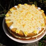 A two layered passionfruit curd sponge cake filled with passionfruit buttercream and topped with orange icing and yellow sugar flowers.