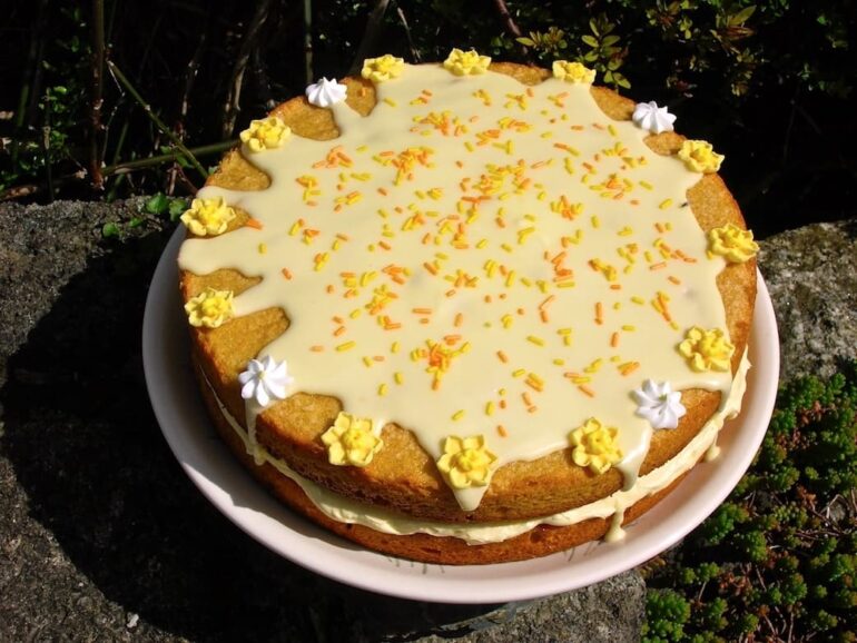 A two layered passionfruit curd sponge cake filled with passionfruit buttercream and topped with orange icing and yellow sugar flowers.