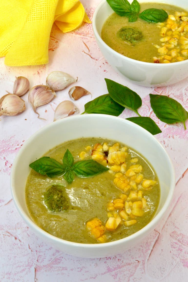 Two bowls of courgette and corn soup with dollop of vegan basil pesto and roasted sweetcorn on top.